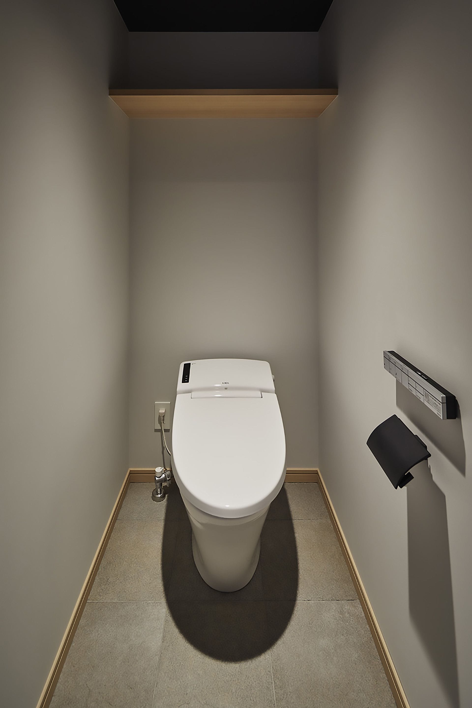 Une salle de bain moderne équipée de toilettes, d’un bidet mural et d’une étagère en bois placée au-dessus des toilettes.