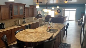 A spacious kitchen with granite countertops, dark wooden cabinets, and a central island with bar stools. There are pendant lights and ceiling fans. - •Lake Erie Vista Dream Penthouse 4 Bed Room 2.5 Bath Private Beach & Indoor Pool (Geneva-on-the-Lake)
