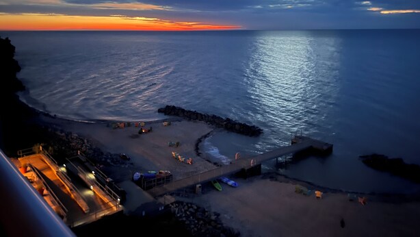 A coastal view with a pier extending into the sea, a sandy beach, and a few tents and boats. - •Lake Erie Vista Dream Penthouse 4 Bed Room 2.5 Bath Private Beach & Indoor Pool (Geneva-on-the-Lake)