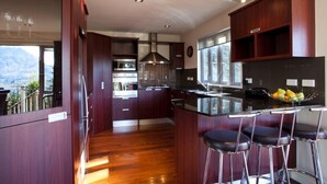 A modern kitchen with dark wood cabinets, a central island with bar stools, stainless steel appliances, and a large window offering a mountain view. - Spectacular Views , Large & Modern , Perfect For Families & Large Groups (Queenstown)