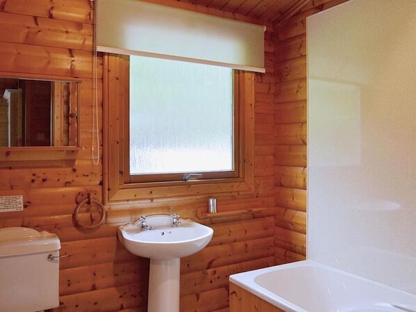 Un baño de cabaña de madera con inodoro, lavamanos y bañera.