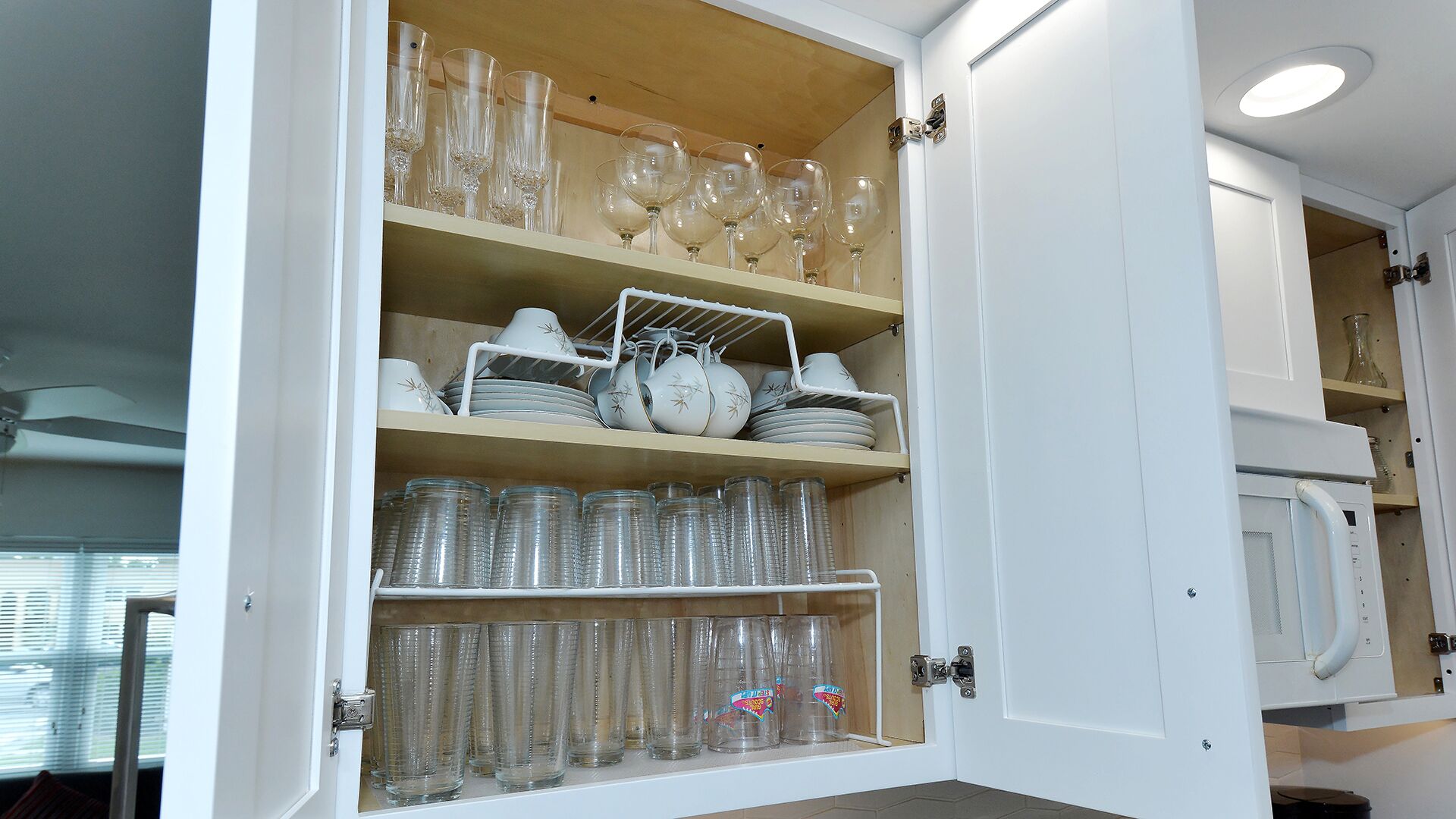 A kitchen cabinet with shelves holding wine glasses, plates, and glassware.