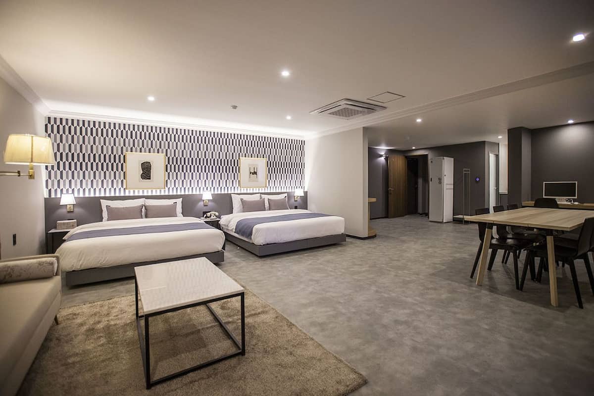 A modern hotel room with two beds, a dining table, and a small seating area.
