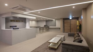 Un moderno vestíbulo de hotel con mostrador de recepción, zona de estar y cocina al fondo.