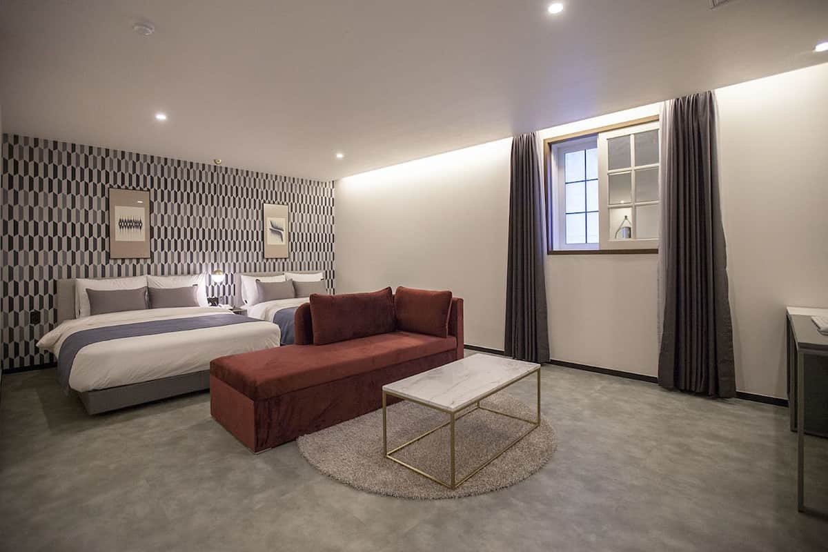 A modern hotel room with a large bed, a red sofa, a marble coffee table, and a patterned wall.