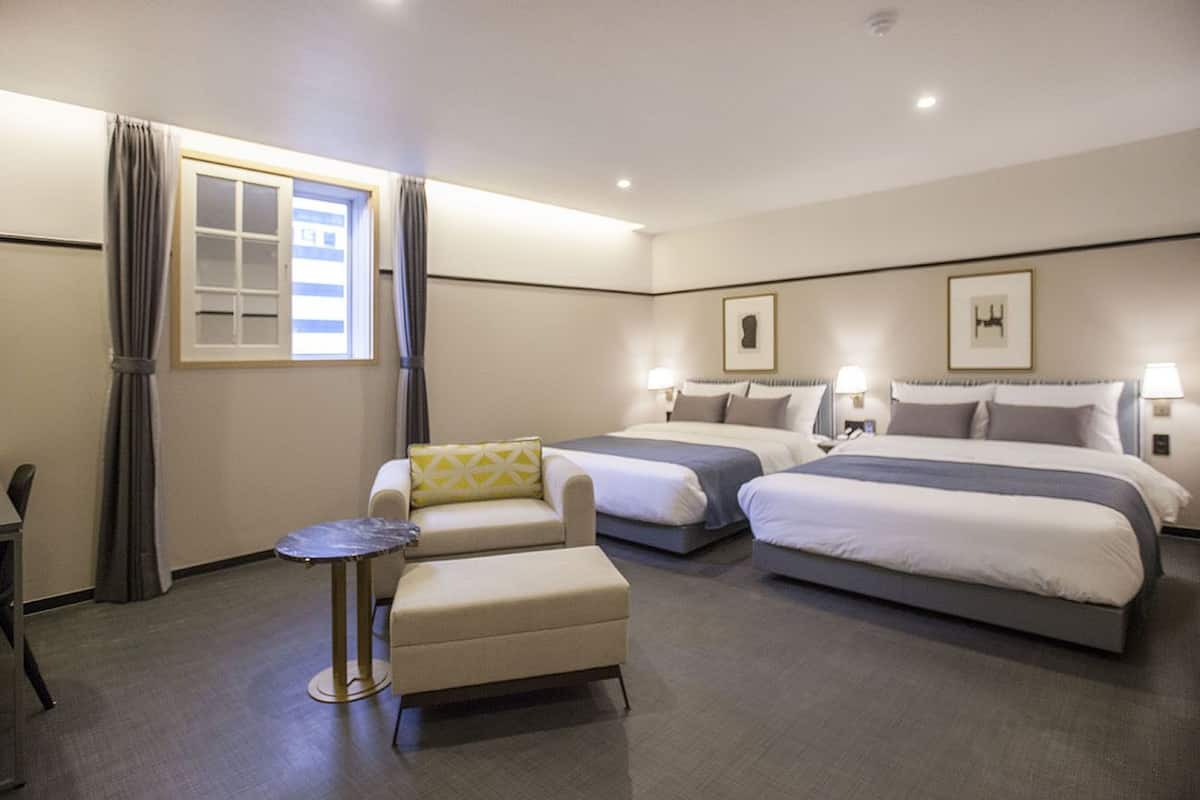 A hotel room with two beds, a sofa, a small table, and a window with curtains.