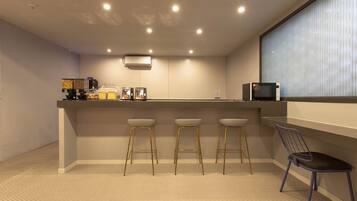 A modern kitchen with a bar area, equipped with a microwave, toaster, and coffee machine. There are three stools and a chair.