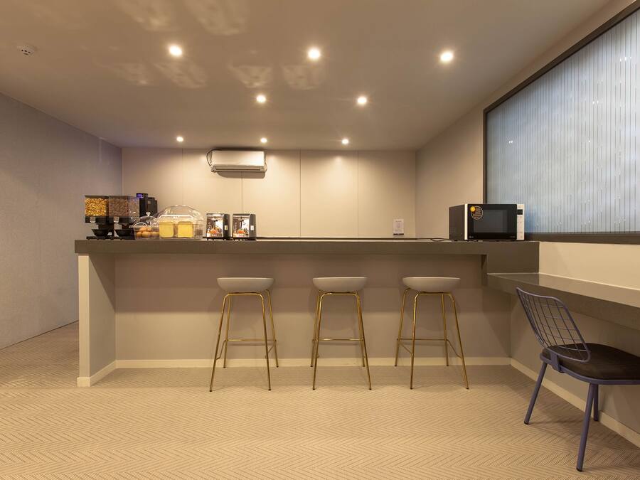 A modern kitchen with a bar area, equipped with a microwave, toaster, and coffee machine. There are three stools and a chair.