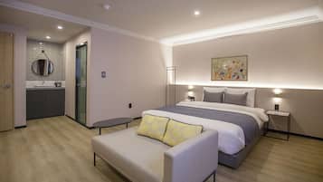 A modern hotel room with a bed, bedside tables, a sofa, a bathroom with a mirror, and a painting on the wall.