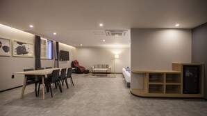 Una habitación moderna y bien iluminada con una mesa de comedor, sillas, un sofá, un televisor y una estantería empotrada.