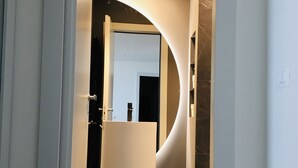 Ein modernes Badezimmer mit einem gewölbten Spiegel, einem weißen Waschbecken und dunklen Fliesen.