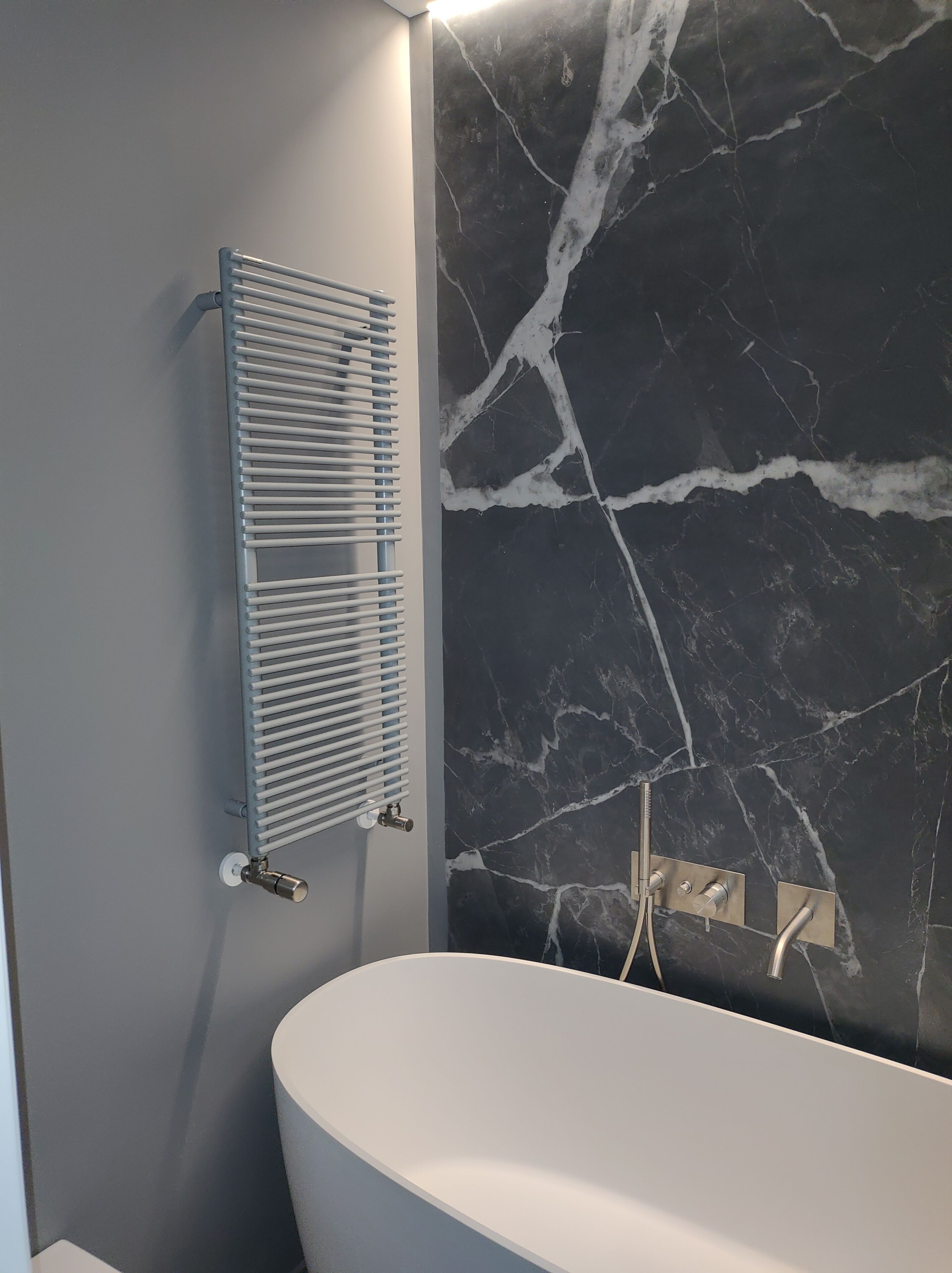 A bathroom with a white bathtub, a wall-mounted towel rack, and a marble-patterned wall.