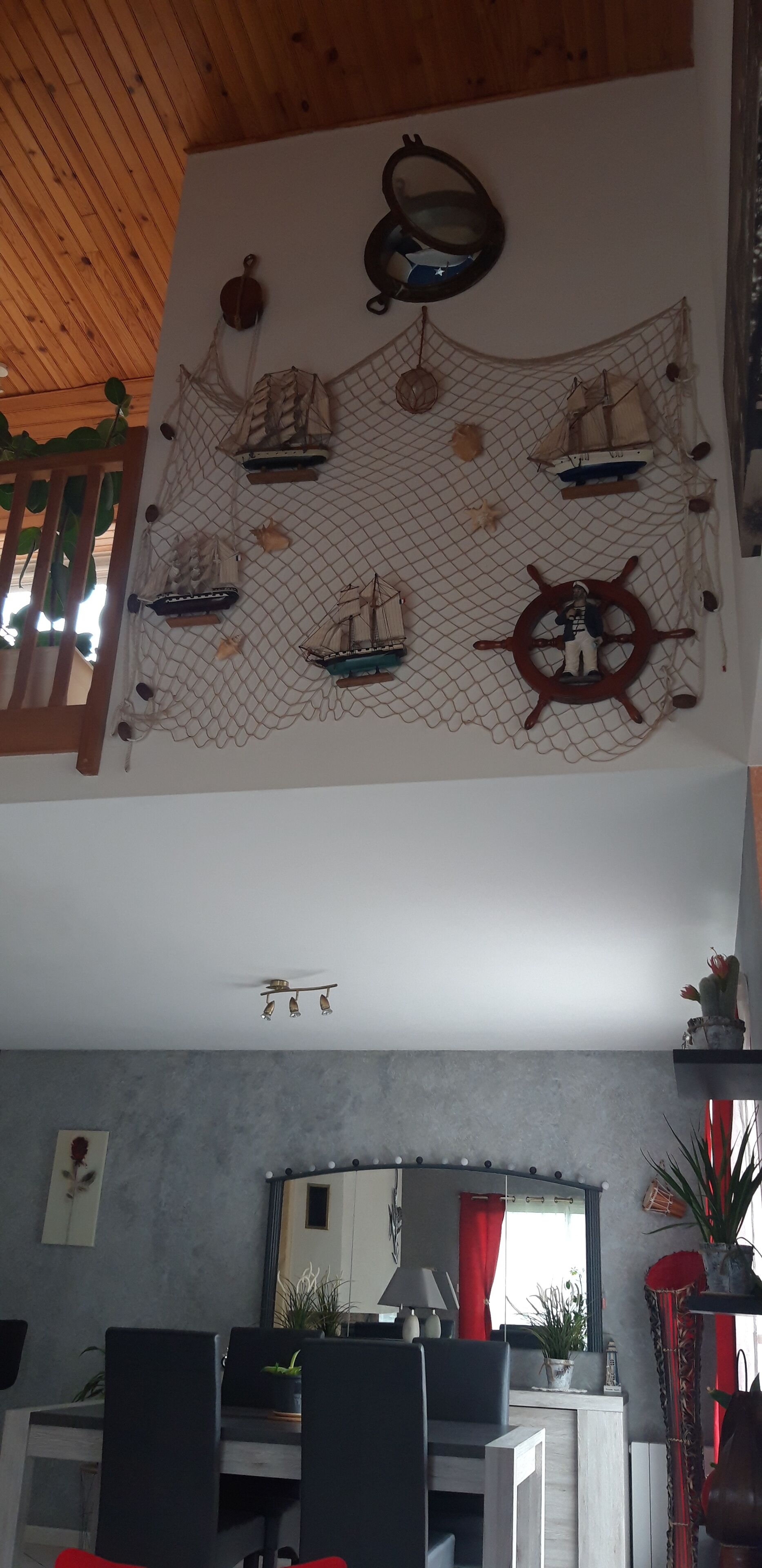 Une pièce avec un plafond en bois, une roue de navire fixée au mur et un motif de voile en forme de filet.