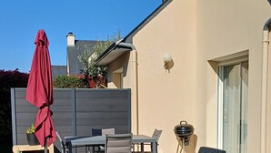 Een terras met buitenmeubilair, een barbecue en een overdekte parasol.