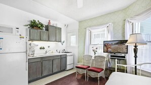 A compact kitchen with a refrigerator, stove, and sink. There are wicker chairs and a television in the room. - 216WA: Budget-friendly Apartment in Victorian Triplex, 2 Blocks to the Beach + W (Avalon)