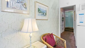 A room with a lamp, framed artwork, a wicker chair, and a door leading to another area. - 216WA: Budget-friendly Apartment in Victorian Triplex, 2 Blocks to the Beach + W (Avalon)