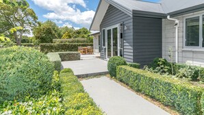 A modern house with a grey exterior, a covered patio, and well-maintained landscaping. - Spacious Modern Two-Bedroom Apartment (Tamahere)