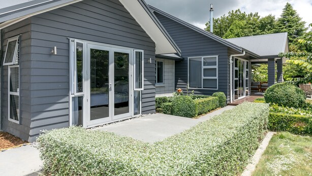 A modern house with a grey exterior, large sliding glass doors, and a well-maintained garden. - Spacious Modern Two-Bedroom Apartment (Tamahere)