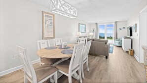 Et spiseområde med et rundt træbord, hvide stole og en moderne lysekrone.