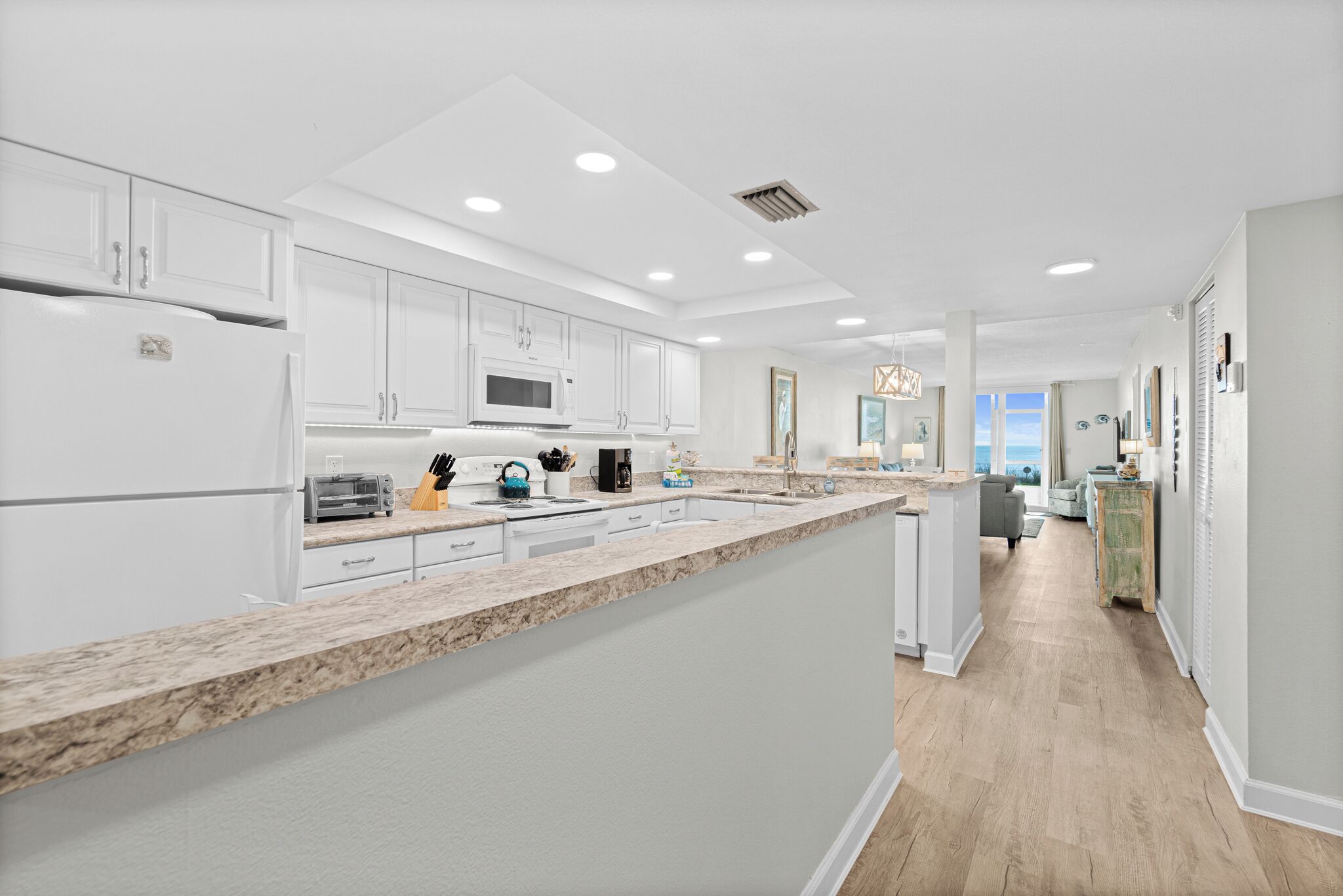 A modern kitchen with white cabinetry, granite countertops, and a view to the living area.