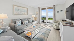 En moderne stue med en grå sofa, et hvidt sofabord og udsigt til det fri gennem en glasdør.