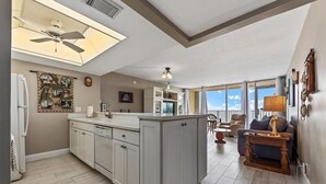 Eine geräumige Küche mit einer zentralen Kochinsel, ein Essbereich mit Ausblick und ein Wohnzimmer mit Sofa und Tisch.