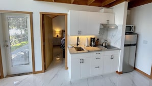 A modern kitchen with white cabinets, a stainless steel refrigerator, a microwave, and a wooden ceiling. - Private Oceanfront Cabin with Hot Tub / Doc Holiday Cabin (Ucluelet)