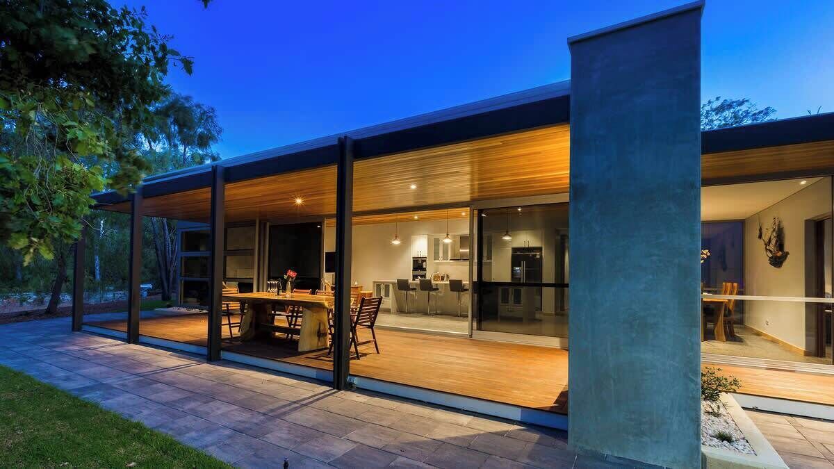 Une maison moderne dotée d’un vaste patio, de grandes fenêtres et d’un intérieur bien éclairé.