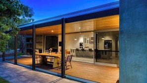 A modern house with a covered patio, a dining area, and a kitchen visible through glass doors.