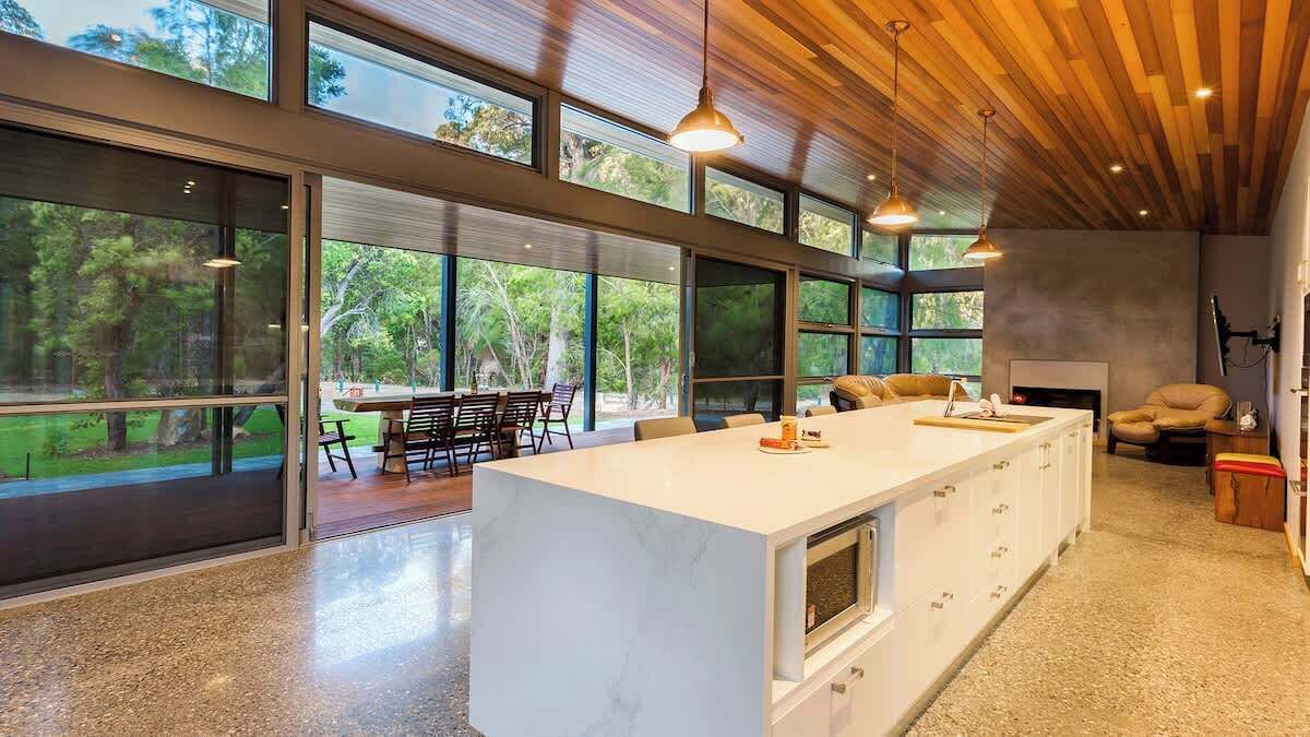 Una cocina moderna con una isla grande, ventanas amplias y un comedor con mesas al aire libre.