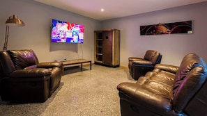 A living room with leather sofas, a flat-screen TV, a coffee table, and a bookshelf.