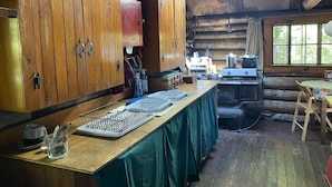 A rustic cabin kitchen with wooden cabinets, a wooden table, and a large window.