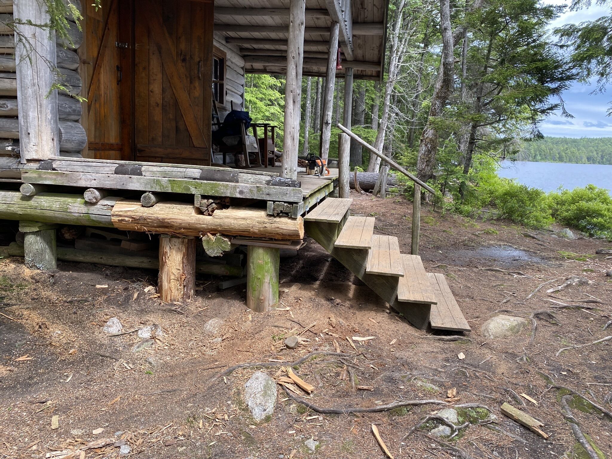 A rustic wooden cabin with a covered porch and a set of wooden stairs leading up to it.