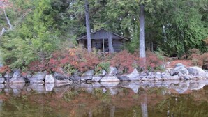 A cabin surrounded by trees and a rocky shoreline.