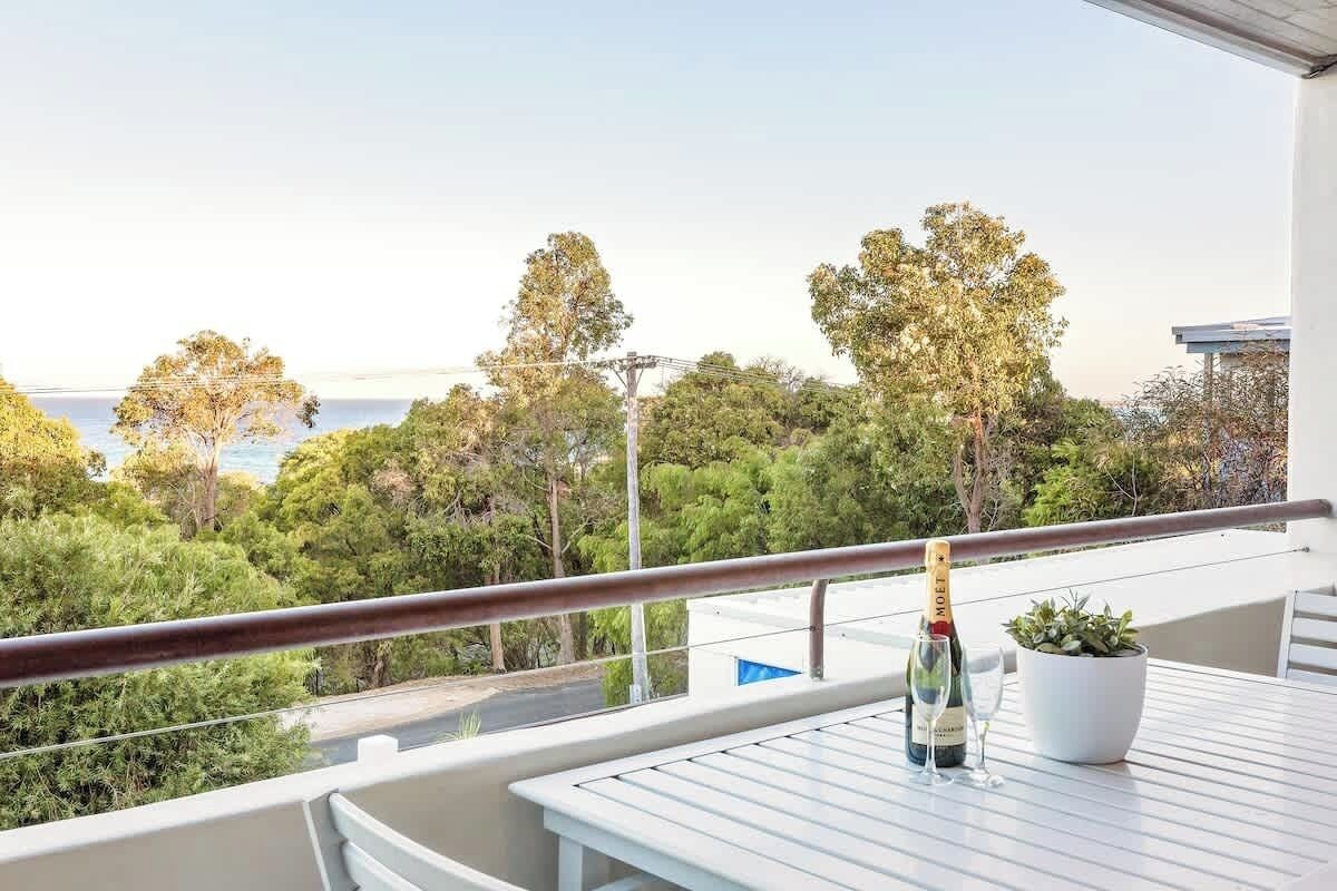 Een balkon met een tafel, een fles champagne en een bloempot.