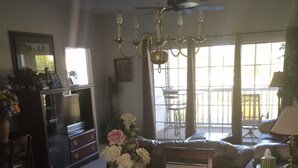 Comedor con una mesa de madera dispuesta para seis personas, rodeada de sillas. Encima de la mesa, hay una araña, y a la derecha, un ventanal con cortinas.