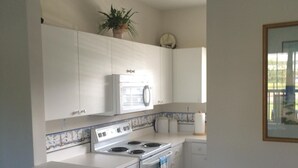 Una cocina con armarios blancos, estufa y microondas. Hay dos taburetes y una planta en la encimera.