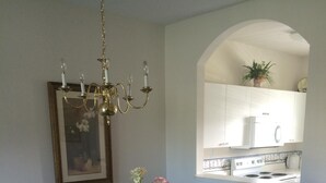 Comedor con una mesa de madera oscura, seis sillas, una araña, un cuadro enmarcado y un jarrón con flores.