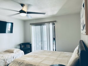 Un dormitorio con una cama, una silla, un ventilador de techo y una ventana con cortinas.