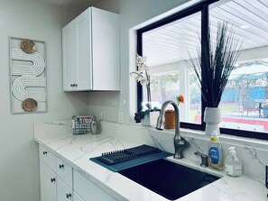 A kitchen with a white marble countertop, a black sink, a stainless steel faucet, and a window with a view of the outdoors.