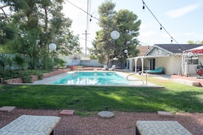 Un patio trasero con piscina, sillas de descanso y un área de patio cubierta.
