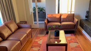 A modern living room with a brown leather sofa, a matching ottoman, and a coffee table with a plant. - Barossa Idyll- Accommodation for Groups (Tanunda)