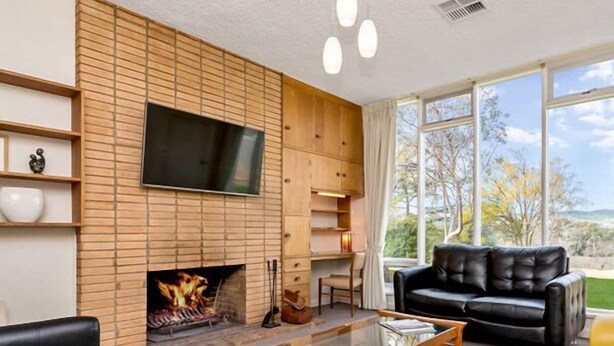 A living room with a fireplace, leather sofas, a coffee table, and a large window offering a view of trees and hills. - Barossa Idyll- Accommodation for Groups (Tanunda)