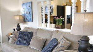 Un salon avec un canapé beige, des coussins à motifs, une table d’appoint avec une lampe et un tableau au mur.