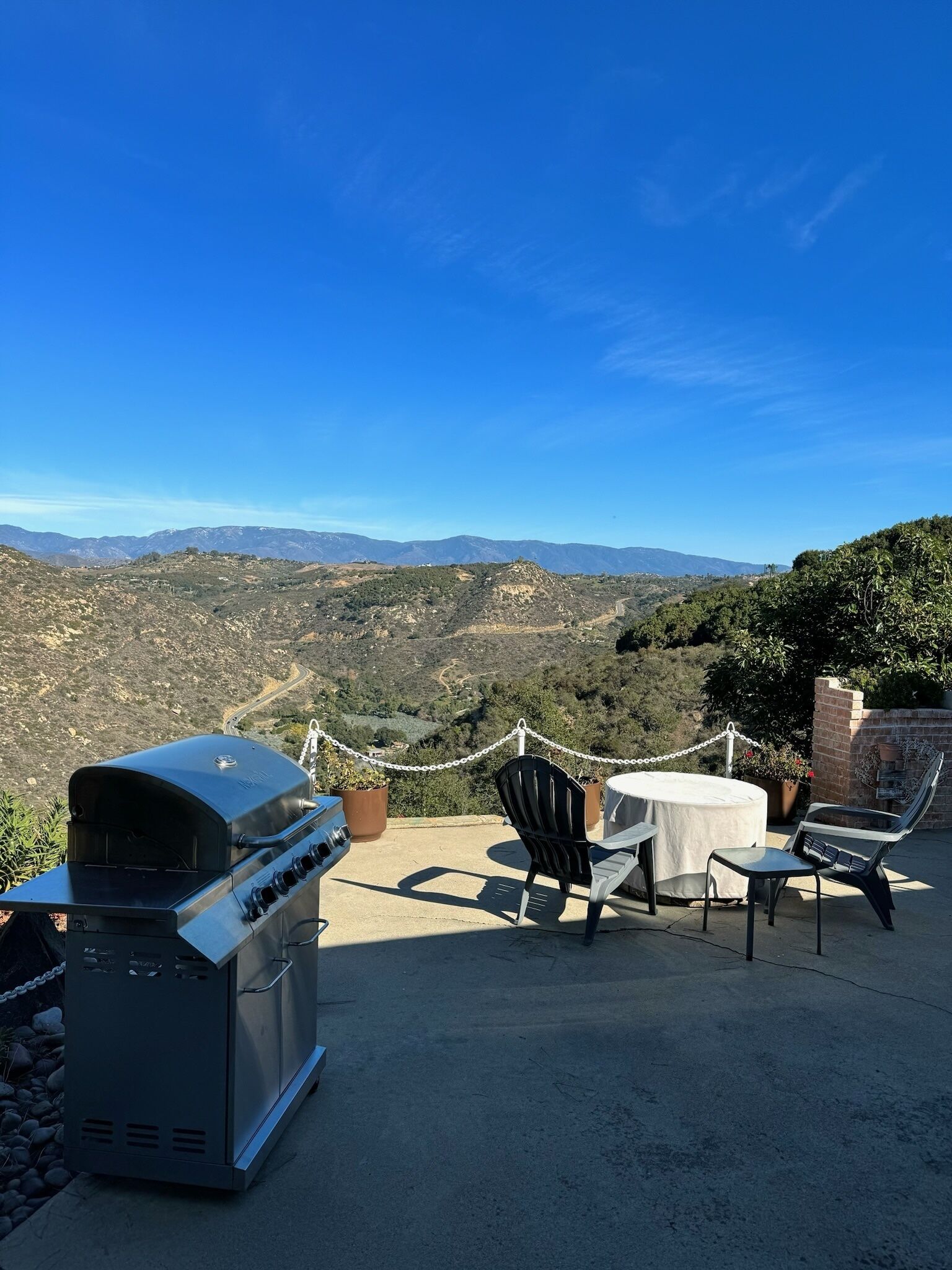 Eine Terrasse mit Grill, Stühlen und Tisch mit Blick auf eine gebirgige Landschaft.