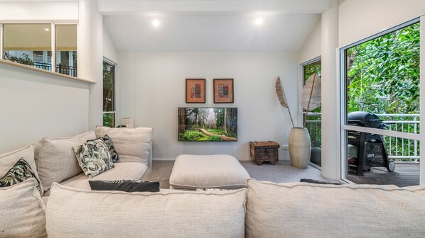 Ein modernes Wohnzimmer mit einem beigefarbenen Sofa, einem Couchtisch und einem großen Fenster mit Blick auf Grünflächen.