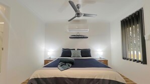Una camera da letto con un letto, due comodini, una ventola a soffitto, un condizionatore e una finestra con persiane.