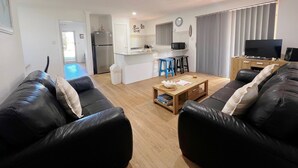 Un appartamento moderno con soggiorno, cucina e sala da pranzo. Sono presenti due divani in pelle nera, un tavolino in legno e una TV.