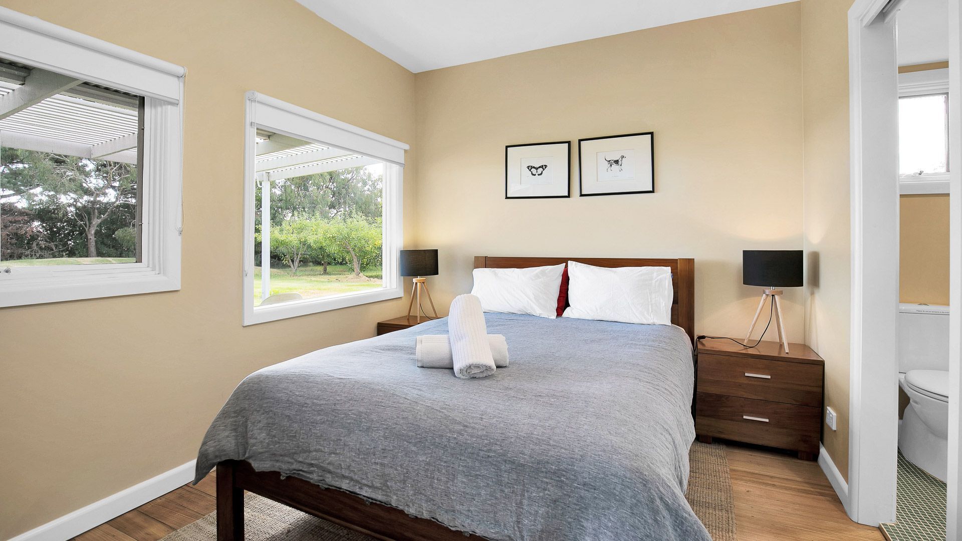 A bedroom with a bed, two bedside tables, a window, and two framed pictures on the wall.