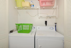 Un espace buanderie équipé d’un lave-linge, d’un sèche-linge et d’étagères où sont rangés des paniers et des produits de nettoyage.